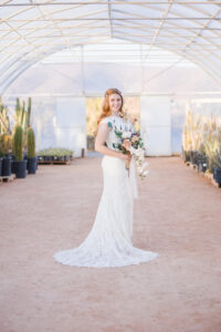 A bride smiles big while holding her bouquet and standing in the cactus joe's wedding greenhouse full of cactus