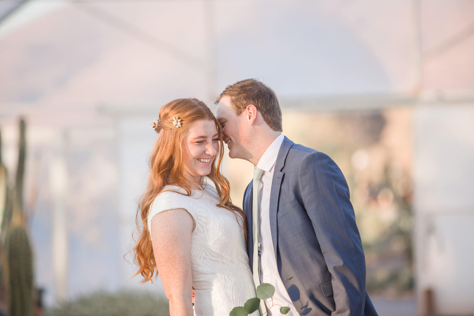 Newlyweds share an intimate laugh while standing in a greenhouse