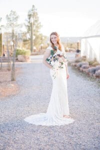 A bride smiles over her shoulder while standing in a gravel garden trail in the desert at her cactus joe's wedding