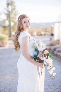 A bride in a lace dress holds her bouquet while standing in a gravel garden trail