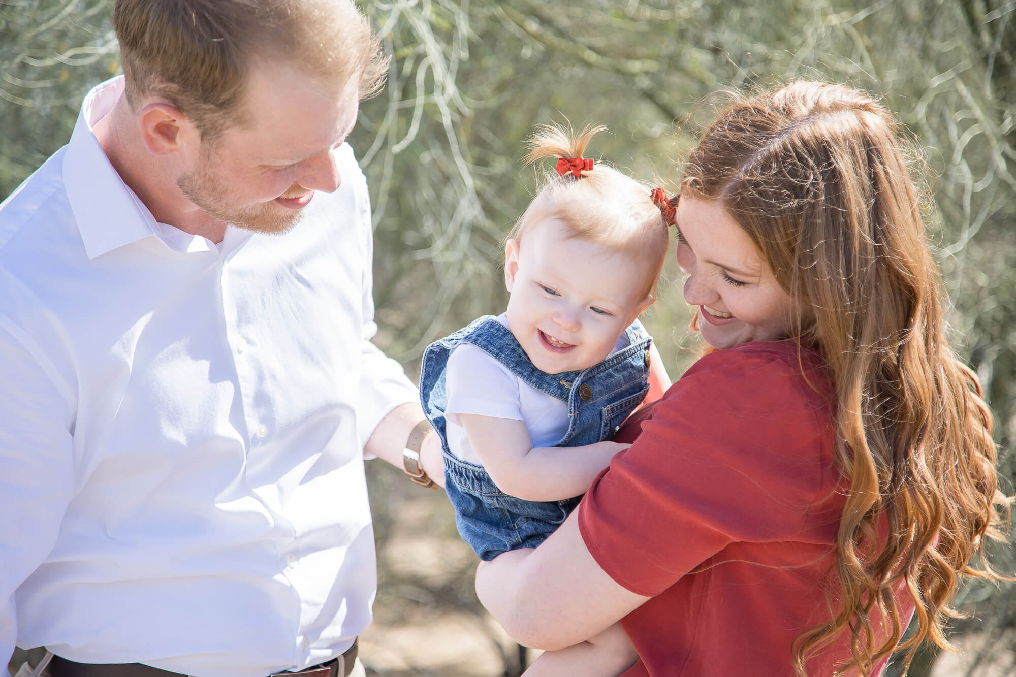 Happy parents play and tickle their toddler daughter in mom's arms while exploring a desert park