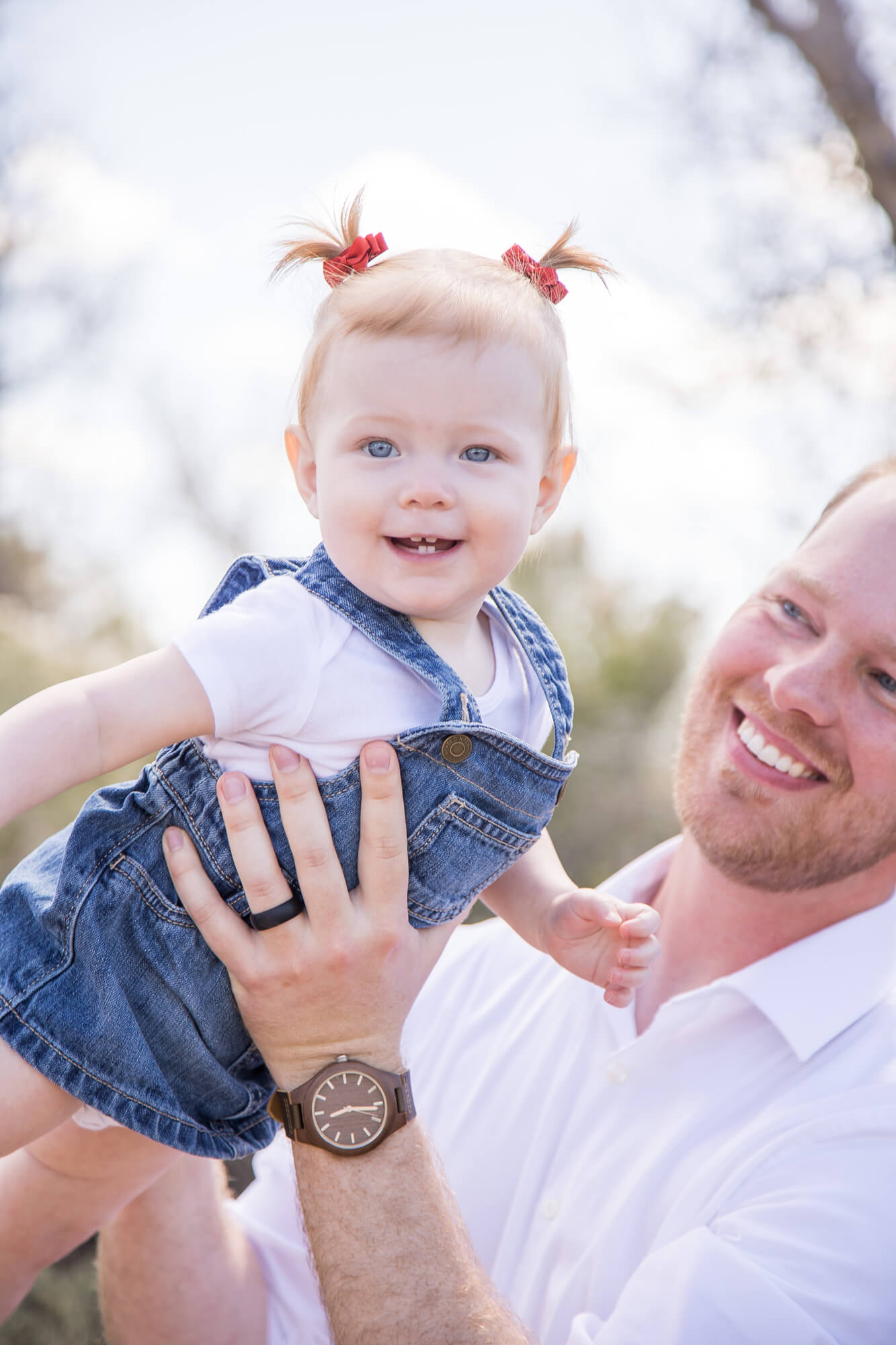 A toddler girl flys with help from dad in her denim overalls in a park during fun things to do in las vegas with kids