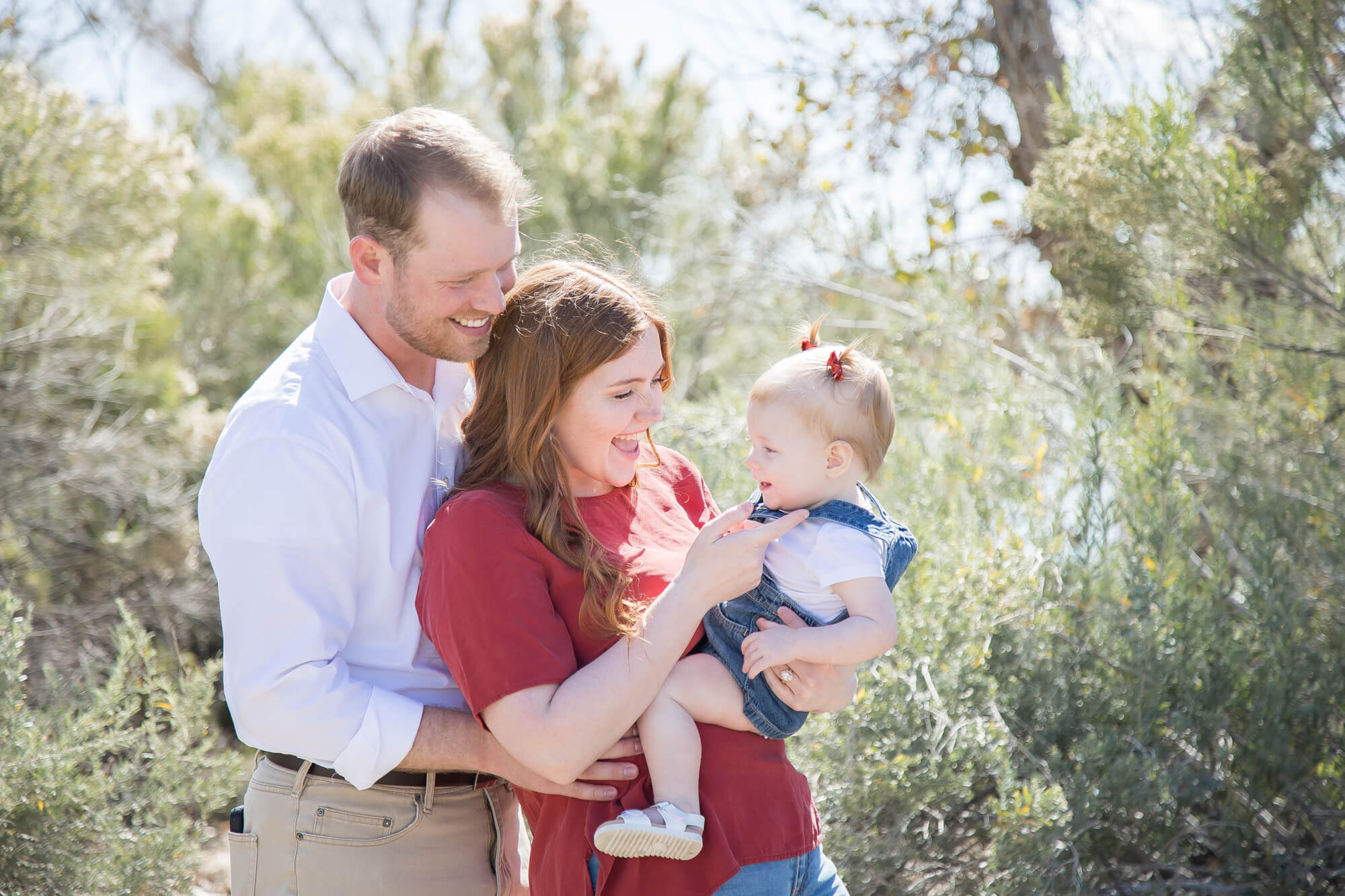 Happy parents laugh and tickle their toddler daughter on mom's hip while standing in a desert park during fun things to do in las vegas with kids