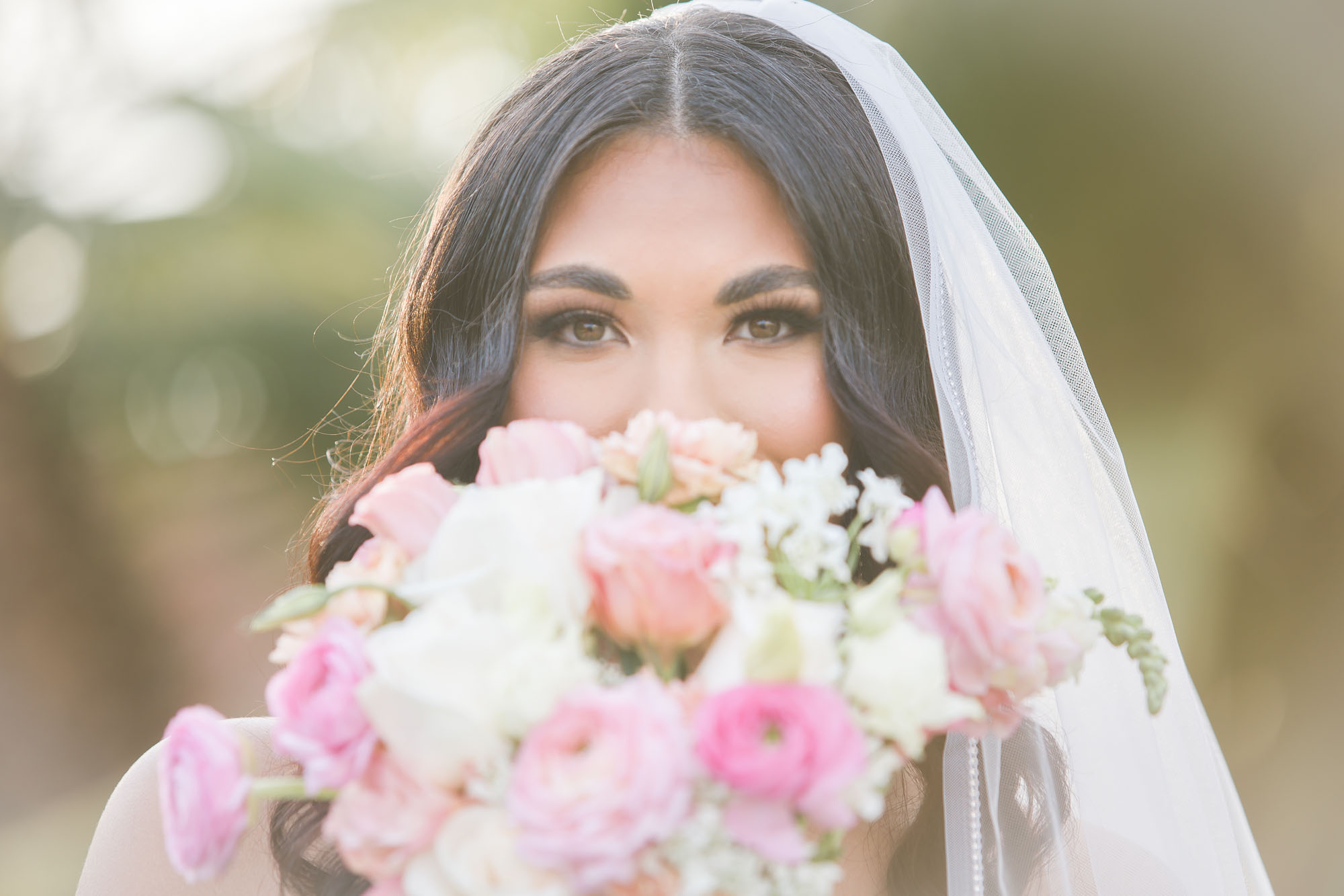 A bride hides behind her colorful bouquet while standing outside at sunset at her las vegas country club wedding