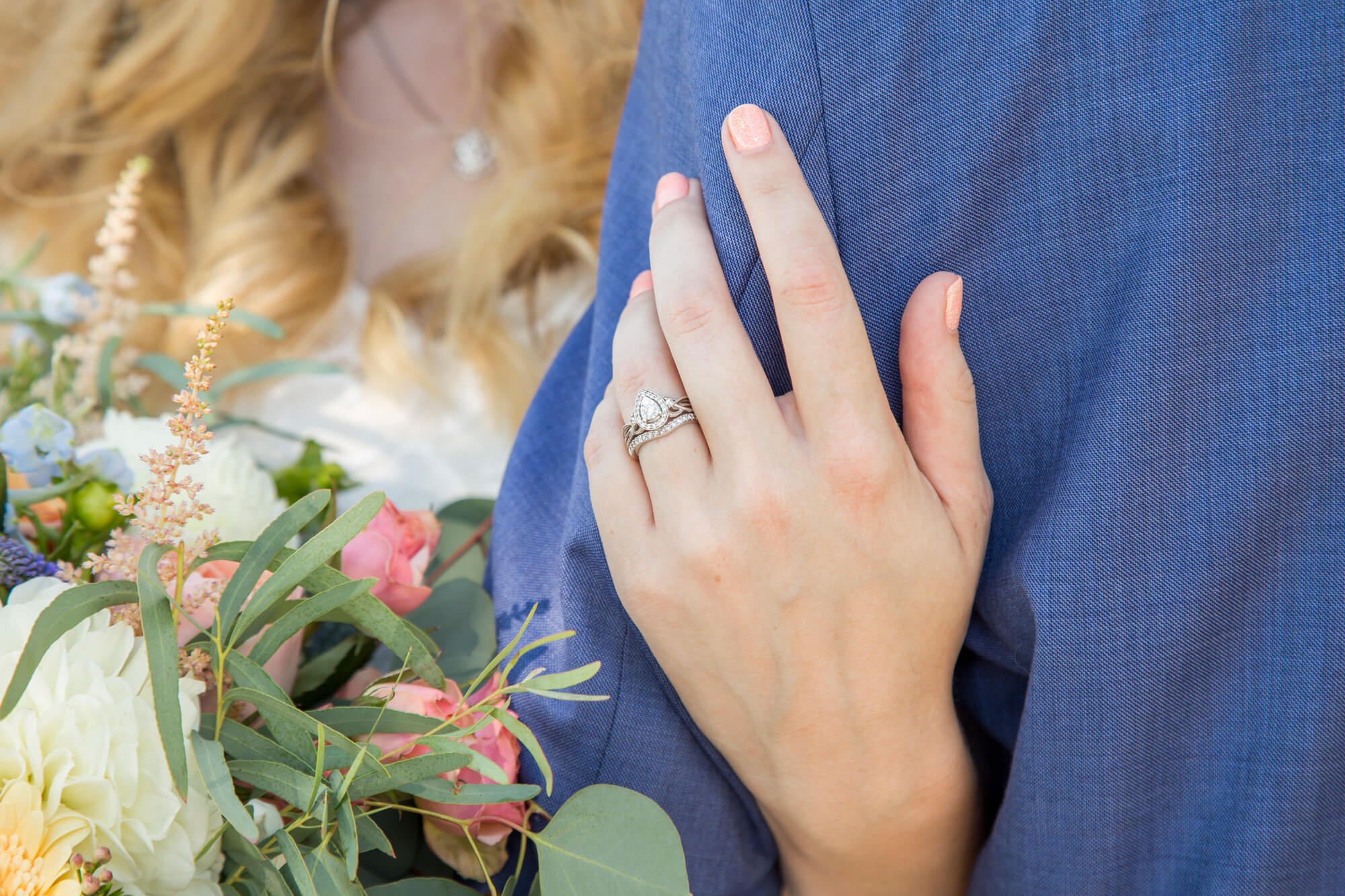 Details of a bride's rings as she holds onto her groom in his blue suit