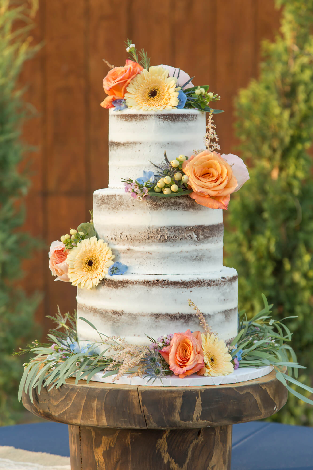 Details of a wedding cake on a wooden stand covered in colorful flowers