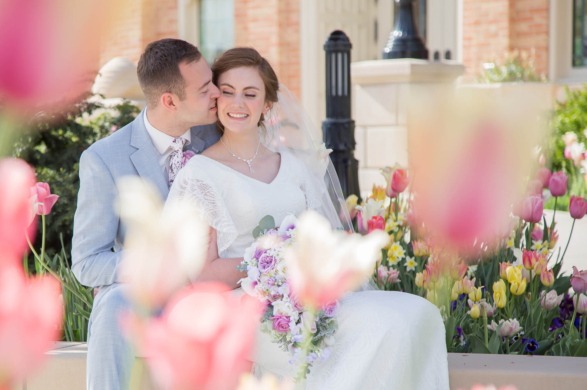 Newlyweds share a quiet moment with a kiss in a light blue suit and lace dress in a colorful tulip garden at one of the las vegas garden wedding venues