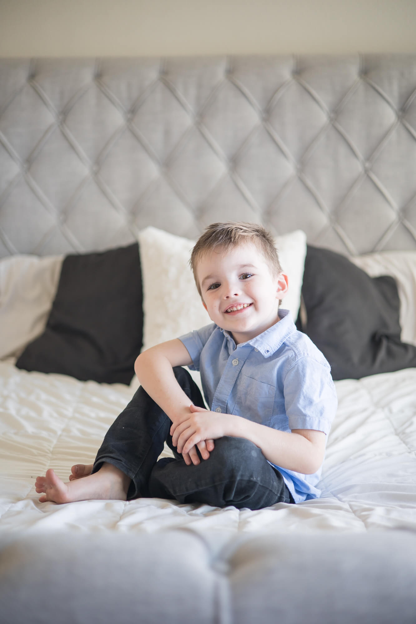 A toddler boy sits on a bed with arms crossed in a blue button down before meeting las vegas nannies