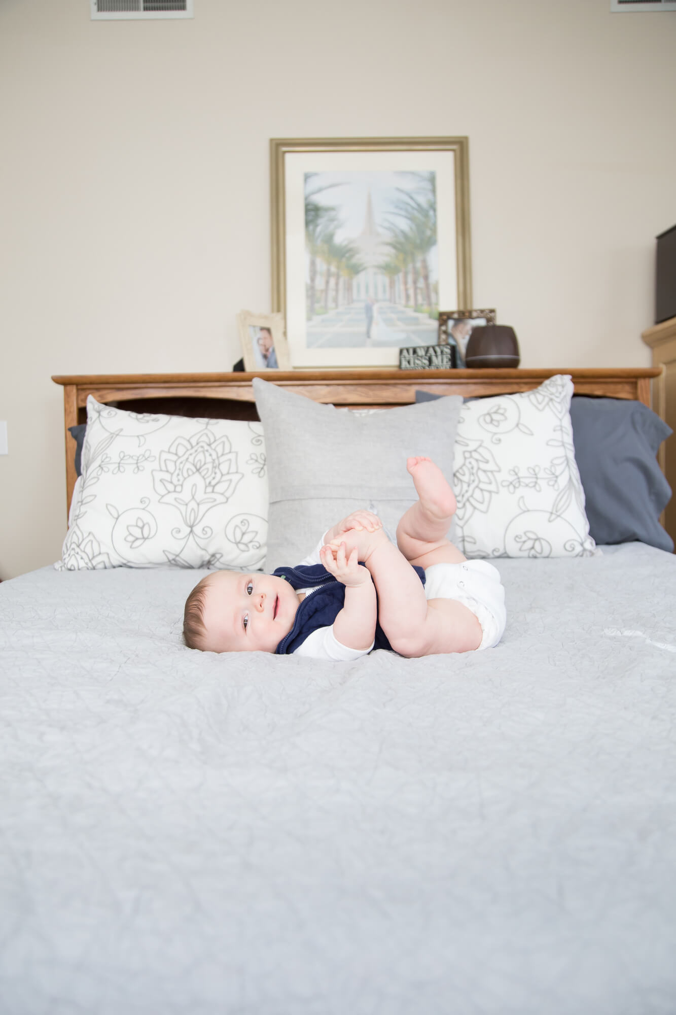 An infant baby boy in a blue sweater lays on a bed playing with his feet before visiting las vegas pediatricians