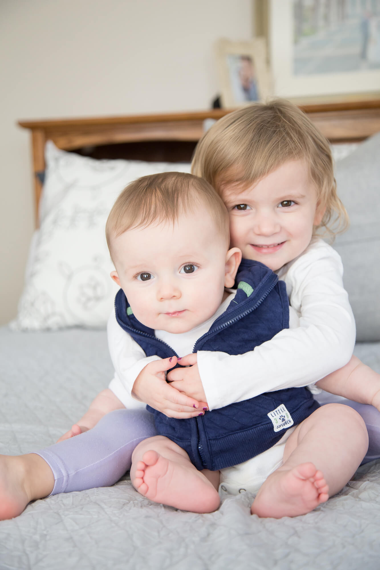 A toddler girl sits on a bed hugging her infant baby brother sitting in her lap before visiting las vegas pediatrician