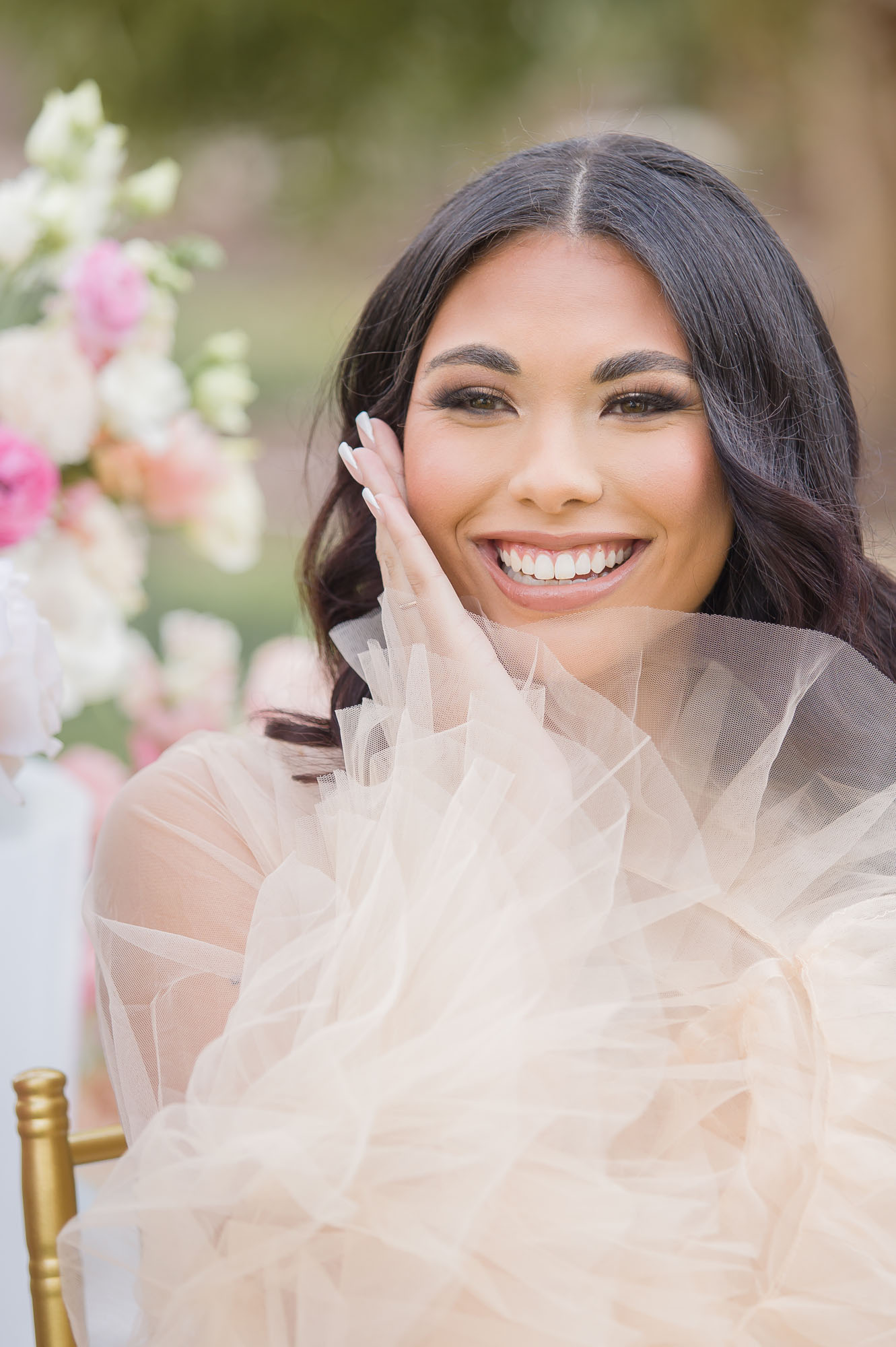 A happy bride smiles big while sitting in a gold chair at her outdoor mansion wedding venues las vegas reception