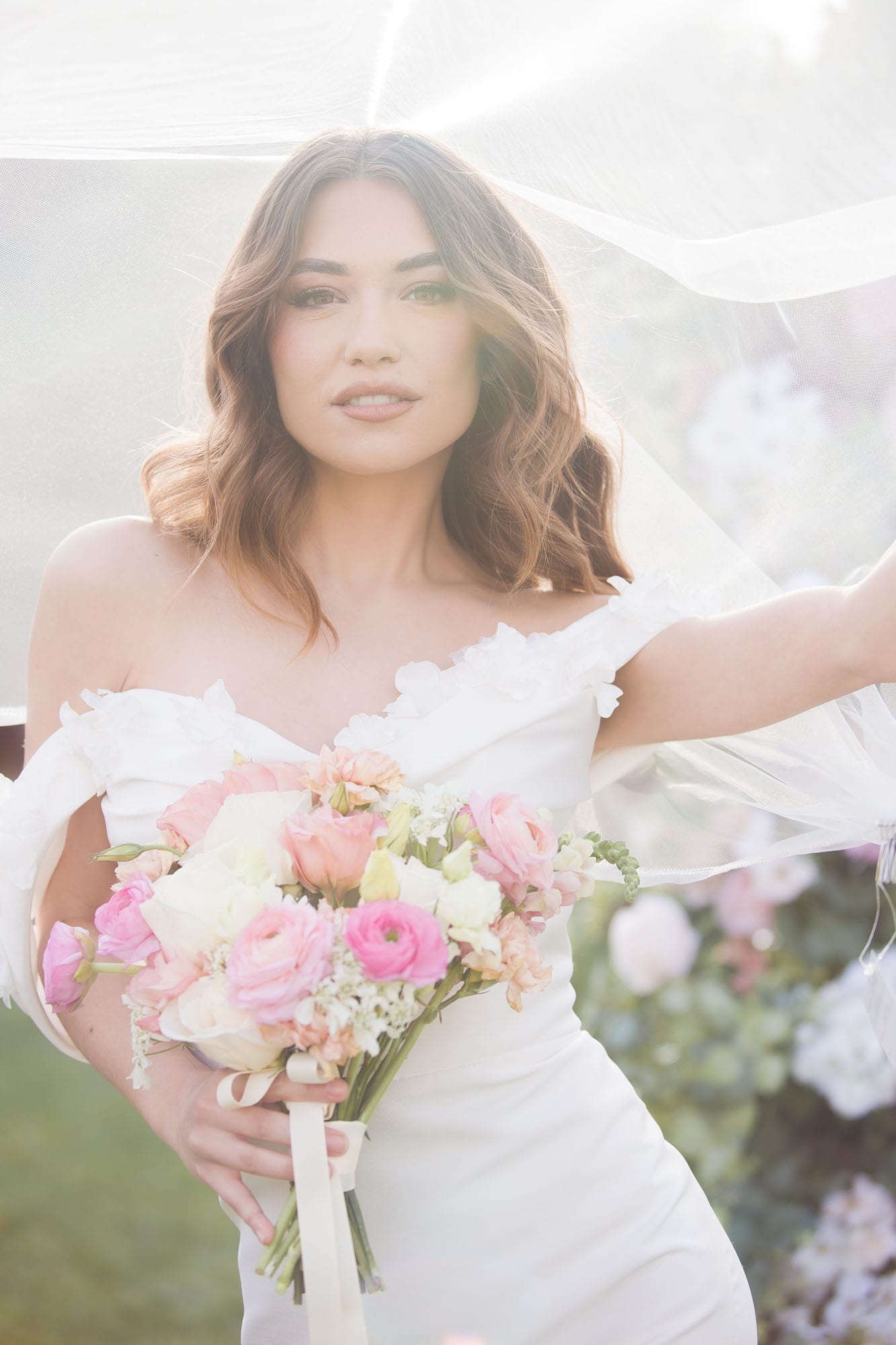 A bride in a silk dress stands in a garden with her veil flowing around her at an outdoor wedding venues las vegas