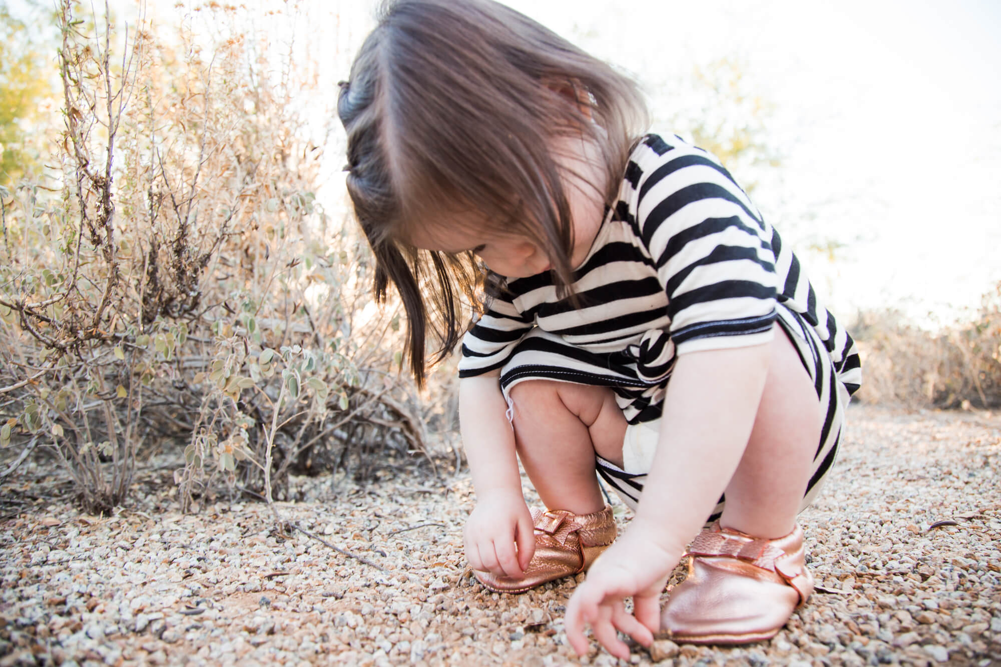 A toddler girl plays in a gravel path in a park