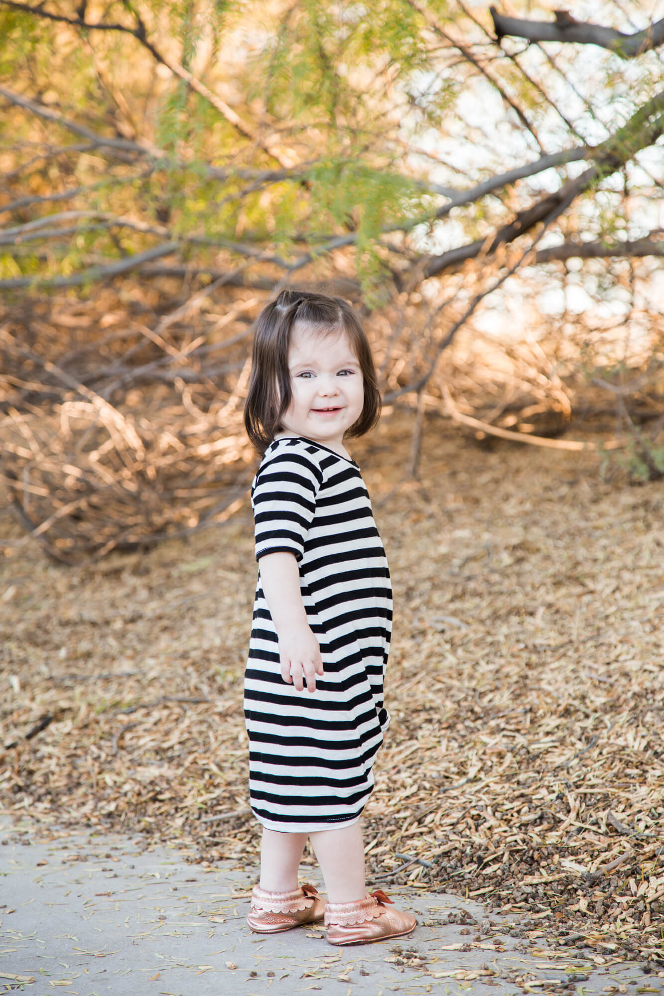 A toddler girl in a striped dress explores a park at sunset before visiting playgrounds in las vegas