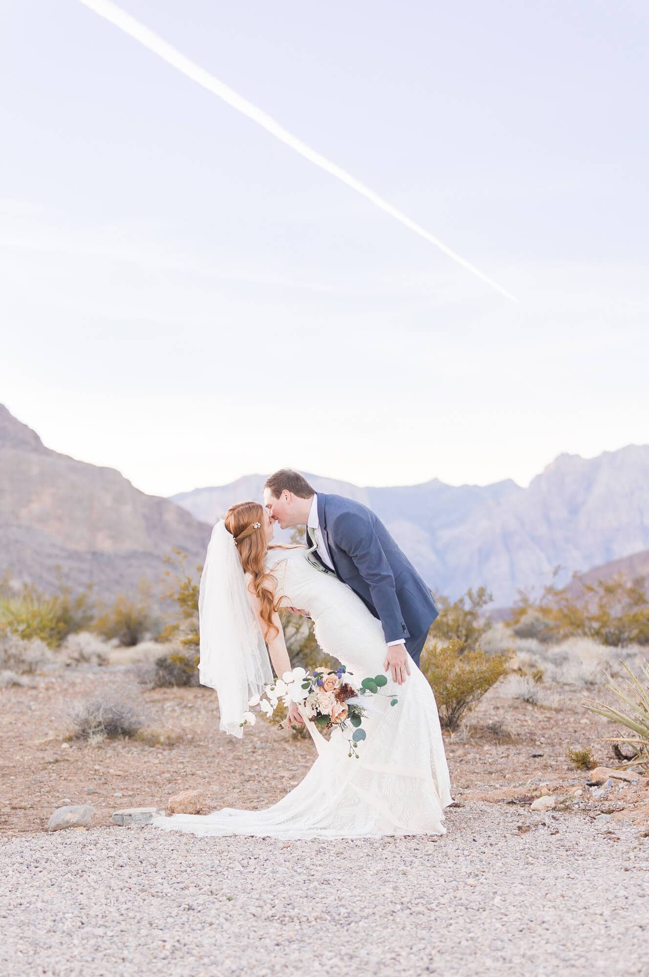 Wedding couple dramatically kisses in front of Red Rock Canyon with a bouquet and veil.